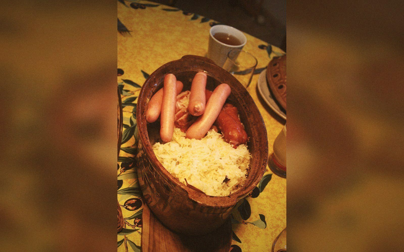 Sausages and sauerkraut served in a rustic ceramic tureen on a patterned tablecloth