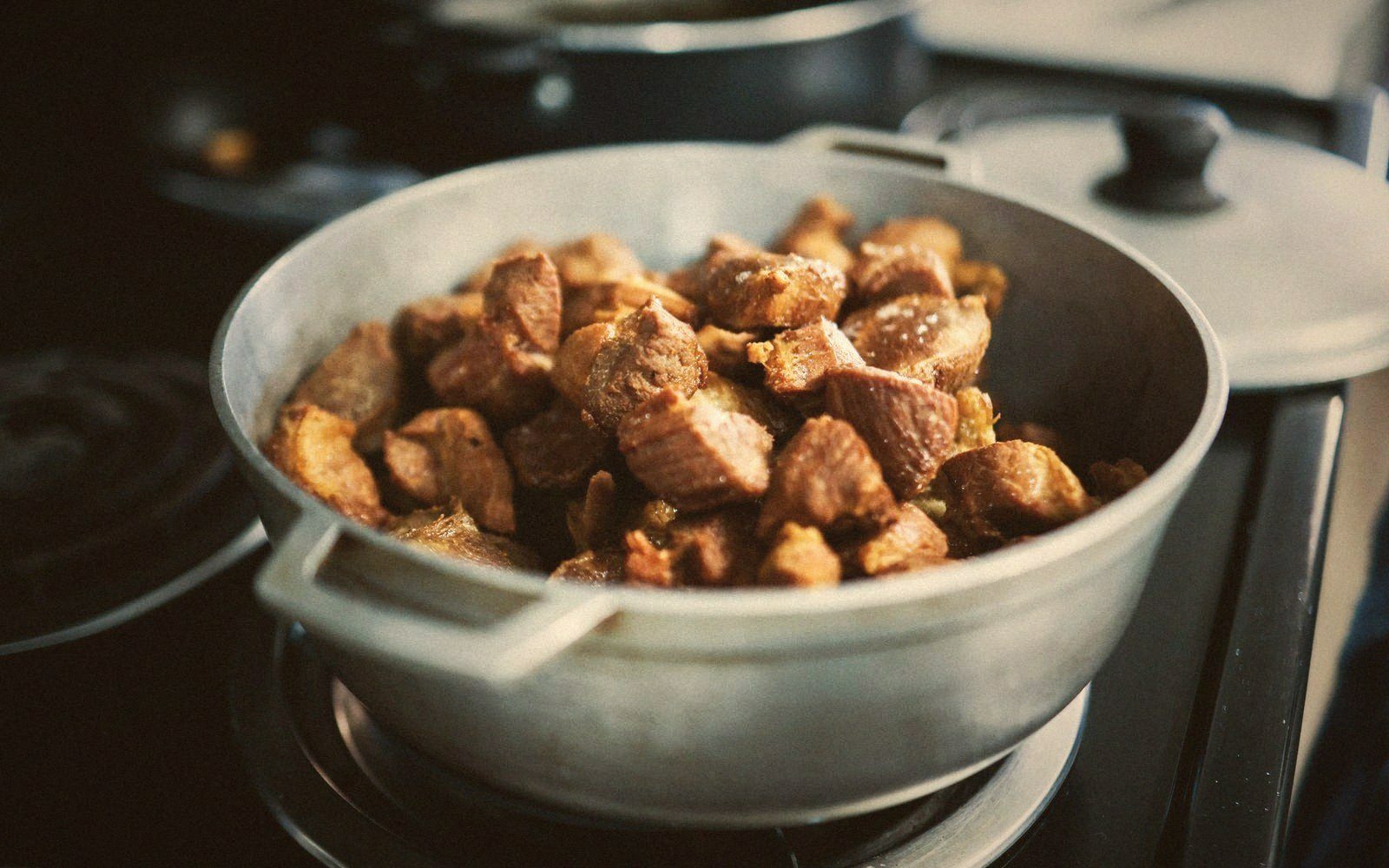 Diced browned meat cooking in a metal pot on a stovetop burner