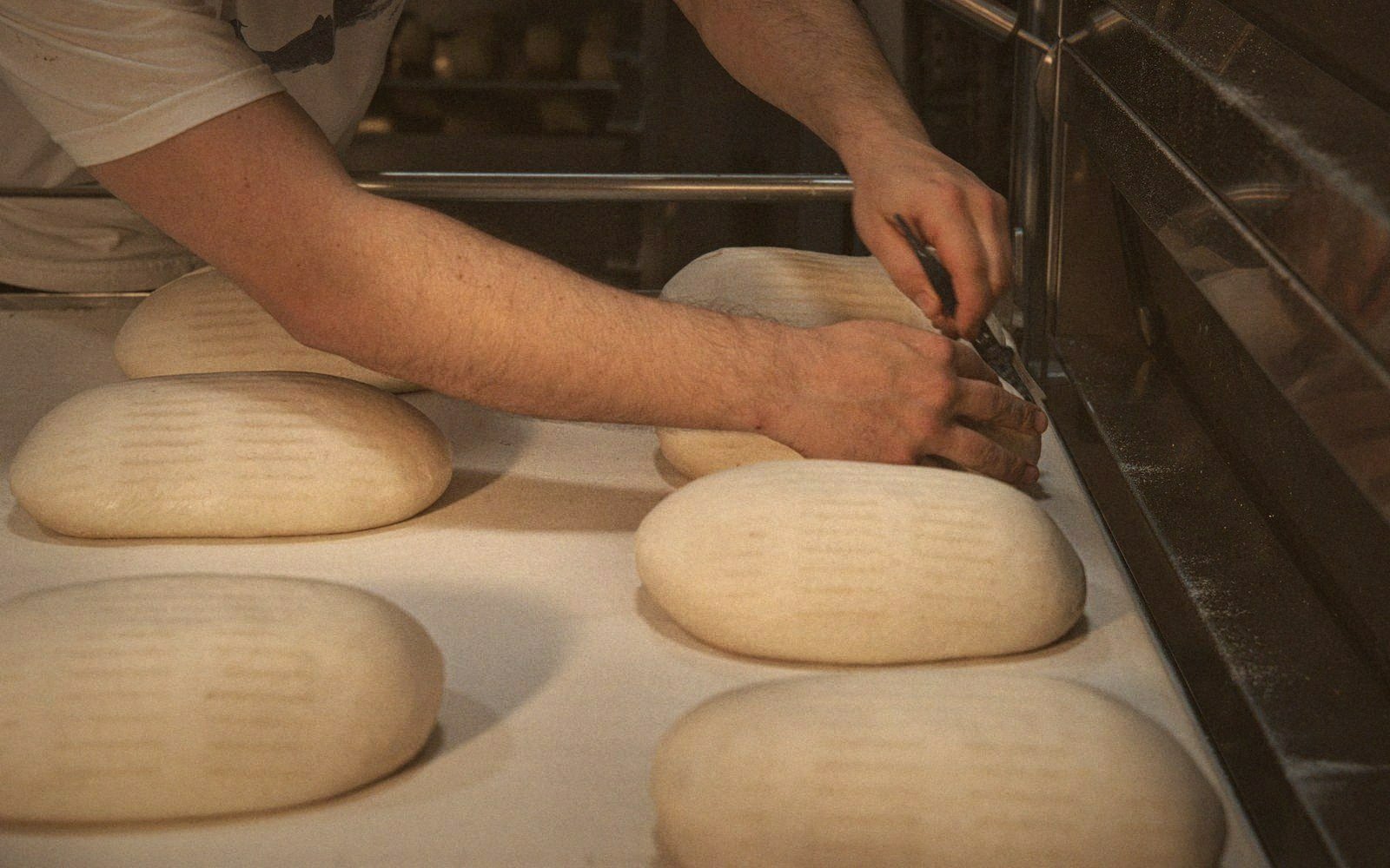 A baker scores raw dough loaves with a blade before placing them in the oven