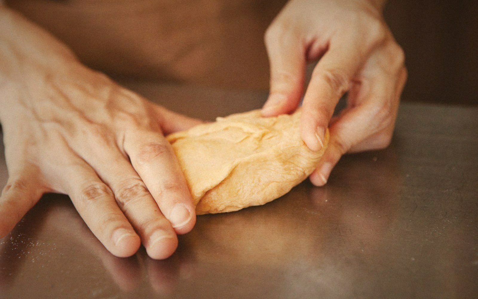 Hands kneading a smooth piece of dough on a metal work surface
