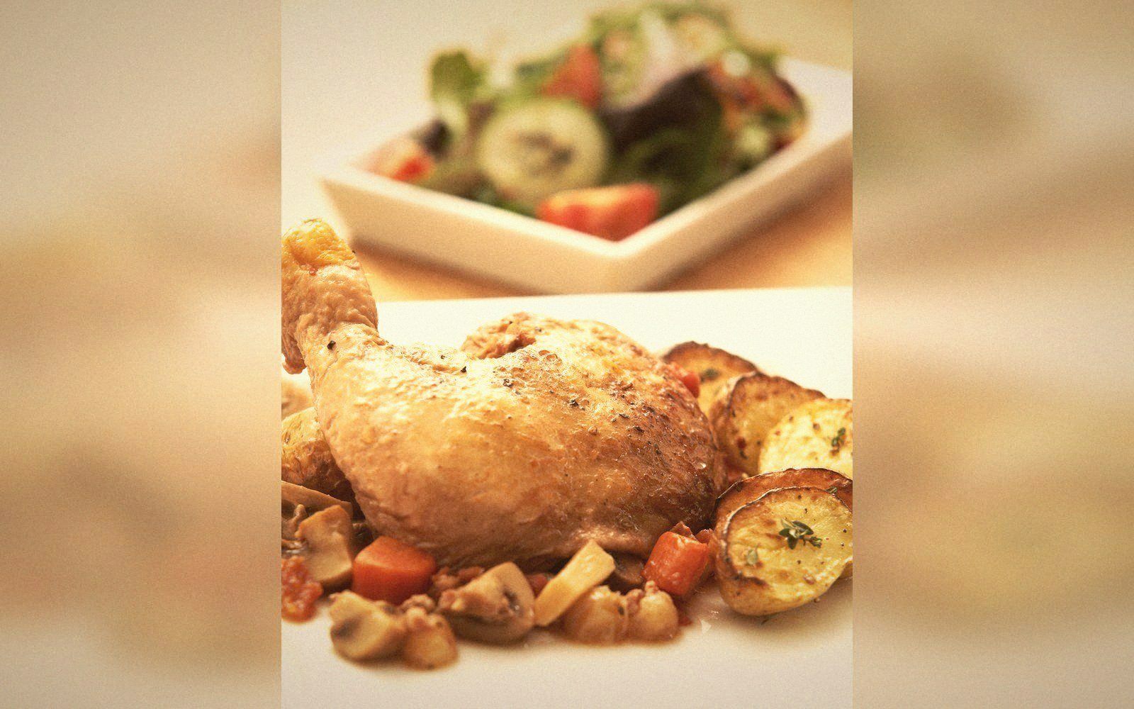 Roasted chicken leg with mushrooms and potatoes, salad plate blurred in background
