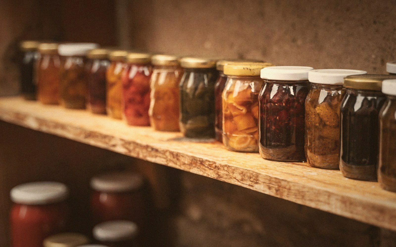 Rows of home-canned fruits and vegetables in glass jars line a wooden shelf