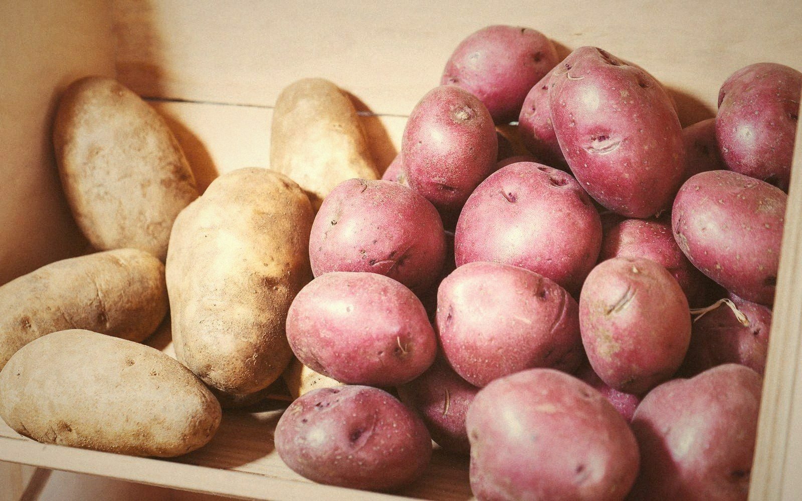 Russet and red potatoes piled together in a wooden crate