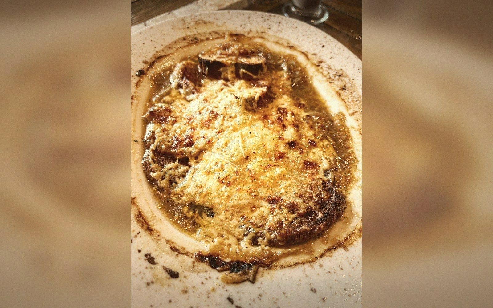 French onion soup topped with melted, browned cheese in a white bowl