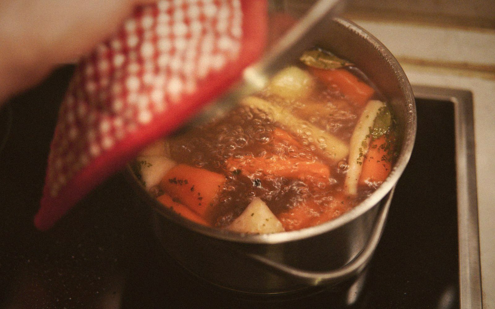 A pot of simmering stock with carrots and herbs bubbling on a stovetop
